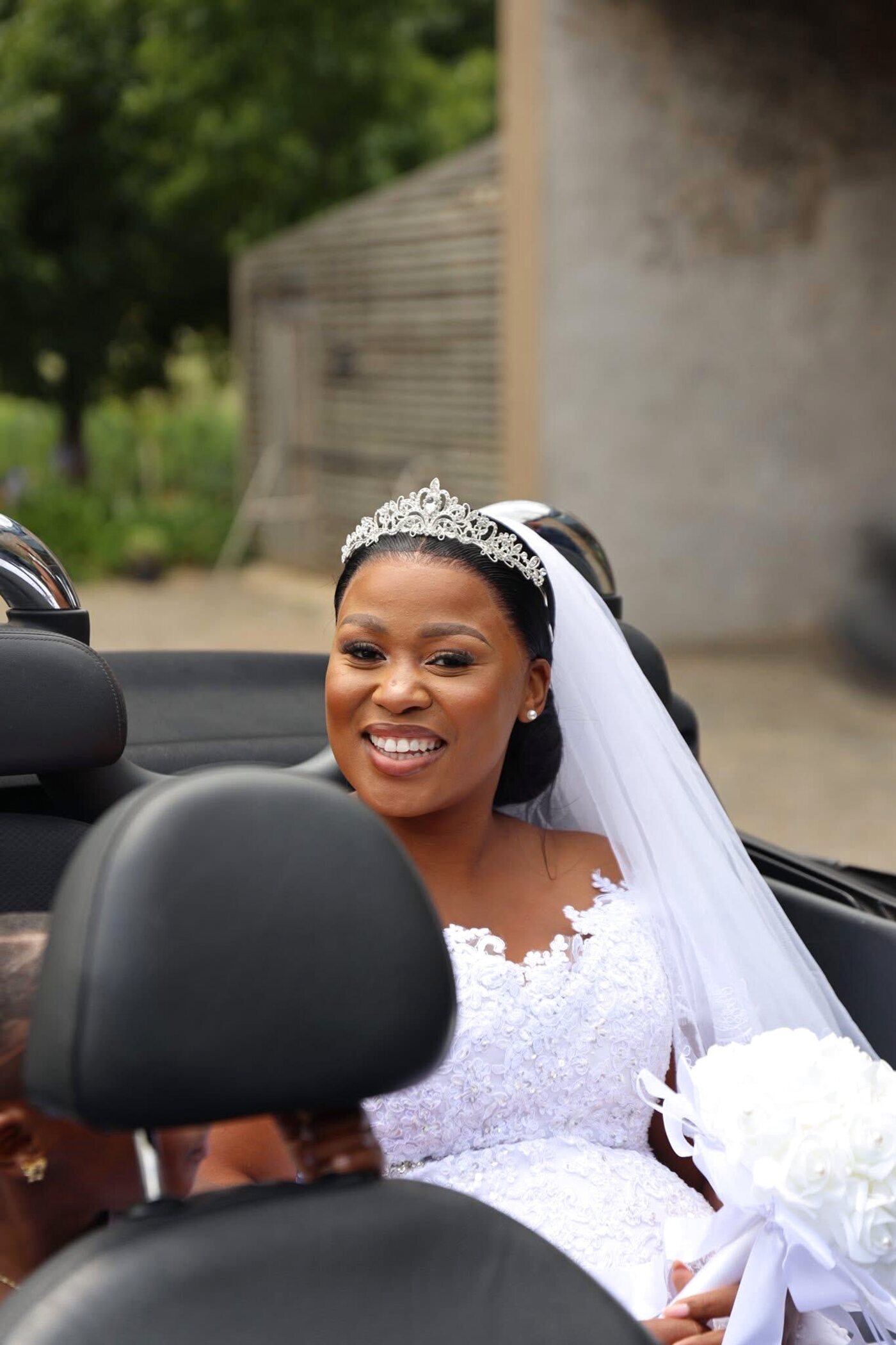 Bride laughing candidly in a car, veil and tiara, soft bridal glam