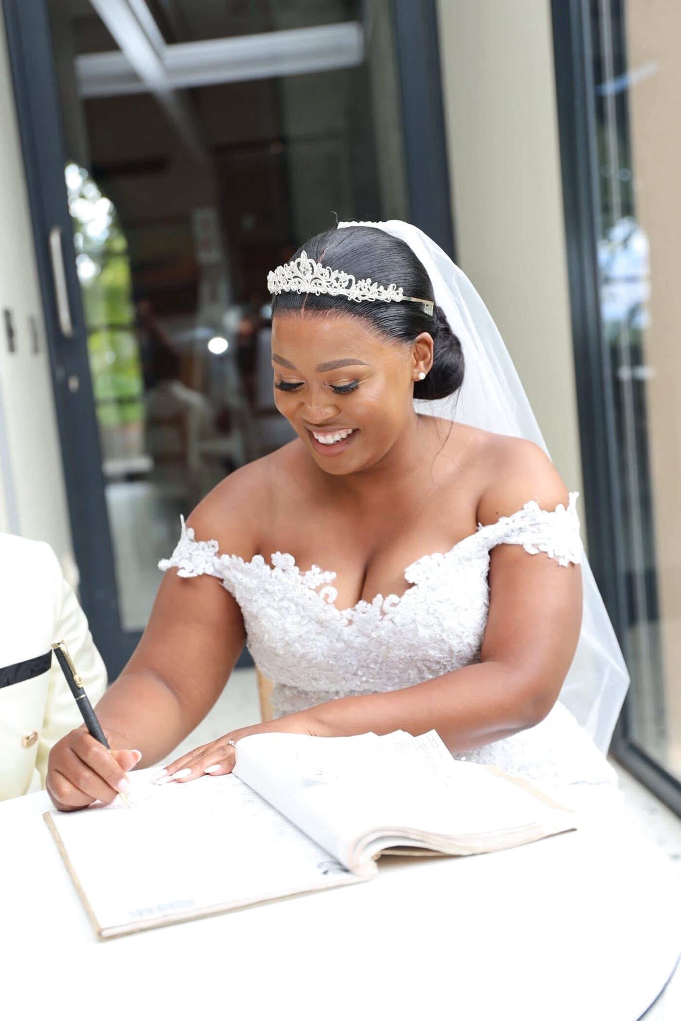 Bride signing the register, off-shoulder gown, long-wear bridal makeup
